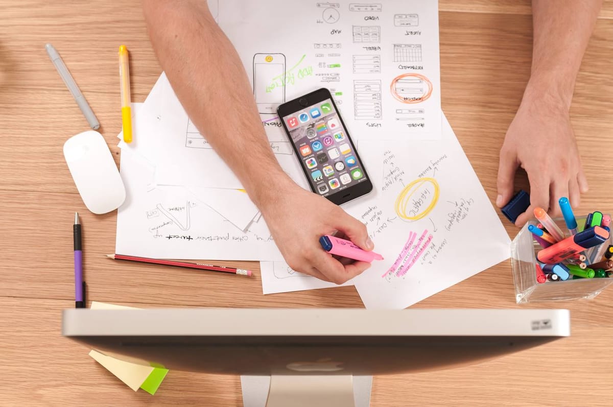 Manos dibujando el diseño de una app en papel junto a un celular